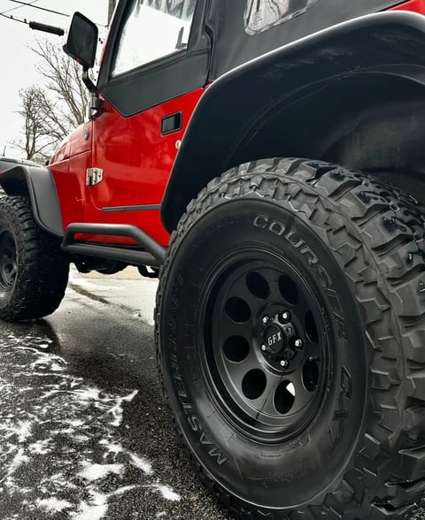 Close-up of red and black Jeep with large all-terrain tires on asphalt pavement