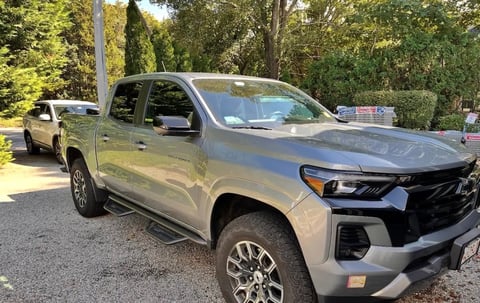 Silver pickup truck parked on gravel driveway with trees in background