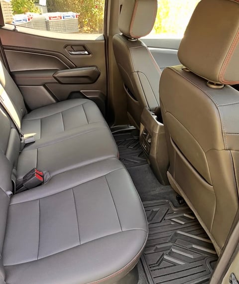 Interior view of a vehicles back seat with gray leather upholstery and black rubber floor mats