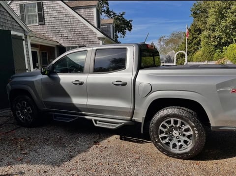 Silver pickup truck parked in front of a shingled house on a gravel driveway