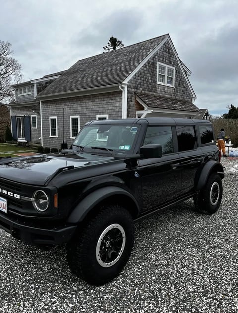 Black Ford Bronco SUV parked on gravel driveway in front of gray shingled house
