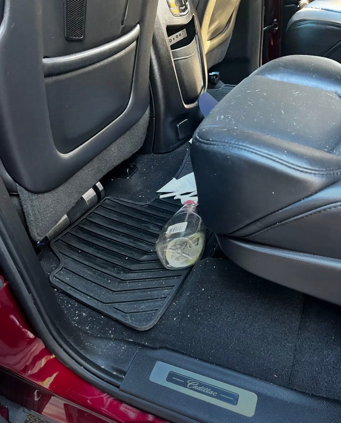 Interior of a vehicle showing a dirty back seat area with a cup on the floor mat and scattered debris
