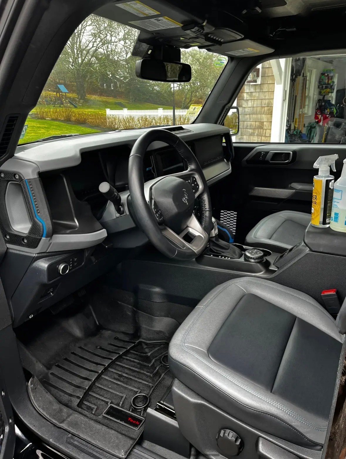 Interior view of a modern SUV dashboard and steering wheel, showing the console, seats, and windshield view of a residential yard and house